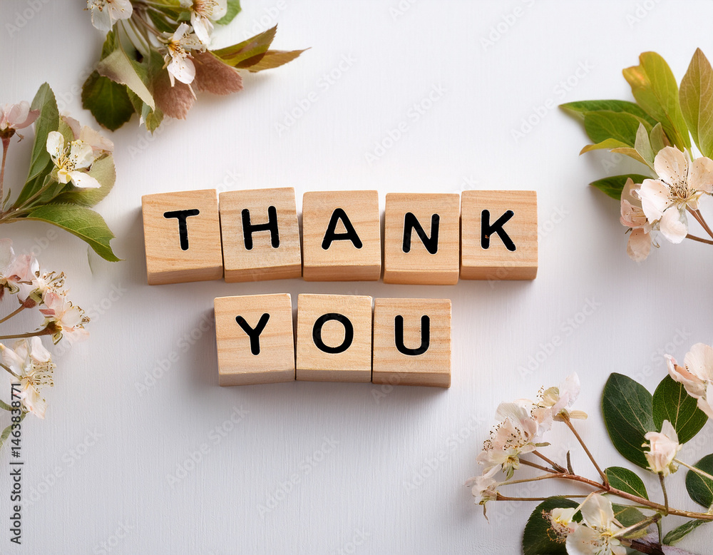 The word THANK YOU written in wooden cubes on a white background with few flowers