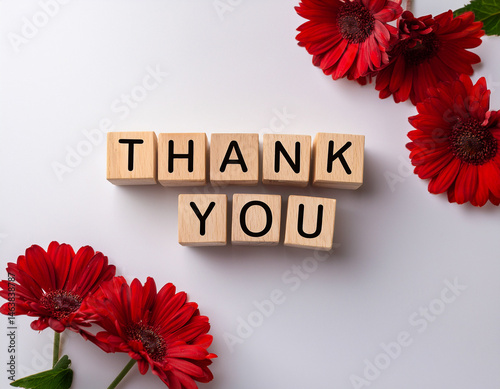 The word THANK YOU written in wooden cubes on a white background with few flowers
