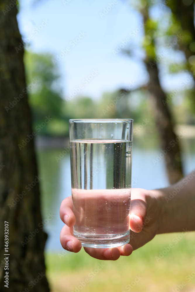 Teenage girl in forest holding glass of clean water in her hand, beautiful spring nature and river, green leaves, landscape
