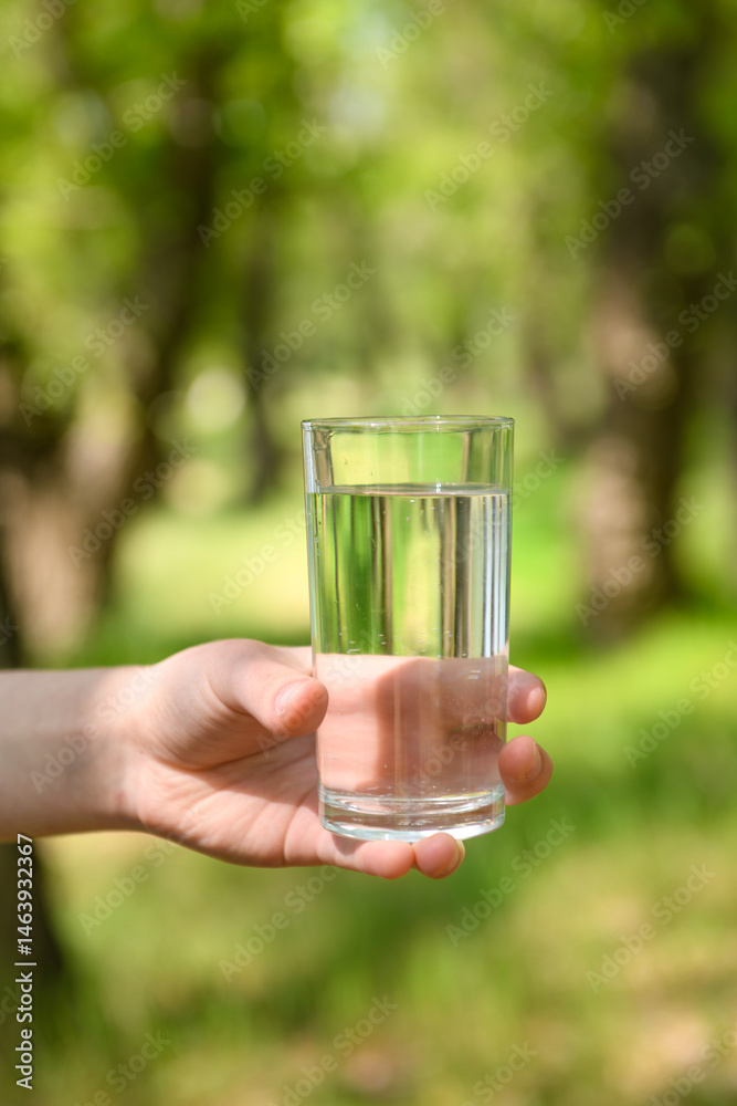 Teenage girl in forest holding glass of clean water in her hand, beautiful spring nature, green leaves, landscape