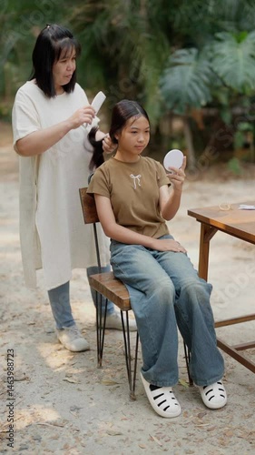 Asian mother braids her daughter's hair