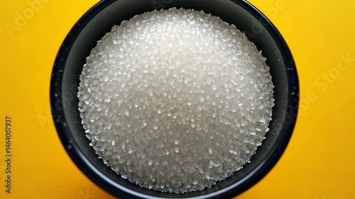 Bowl of coarse sea salt on solid yellow background. 