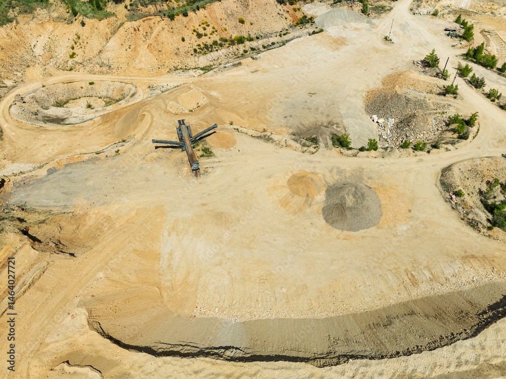 Aerial drone view of sand or gravel quarry surrounded by forest and farmland with distant hills. Aerial Drone view shows an inactive or abandoned quarry embedded in a green landscape.