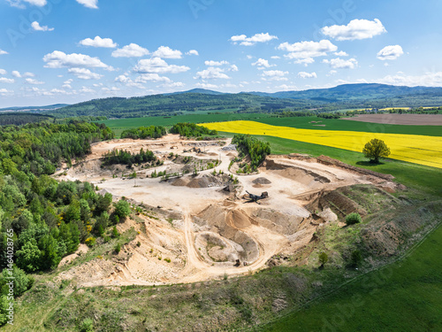 Obraz na płótnie Aerial drone view of sand or gravel quarry surrounded by forest and farmland with distant hills. Aerial Drone view shows an inactive or abandoned quarry embedded in a green landscape. w salonie