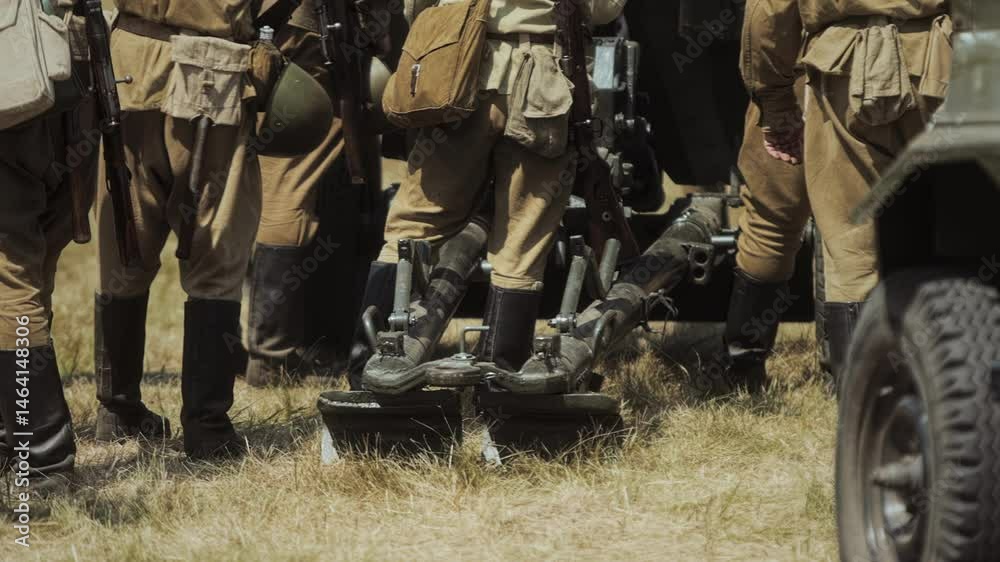 Reenactment portrays Soviet forces during Great Patriotic War. Participants stand near field artillery 82mm mortar, likely BM-37 model piece WWII era. Men wear authentic Red Army uniforms boots