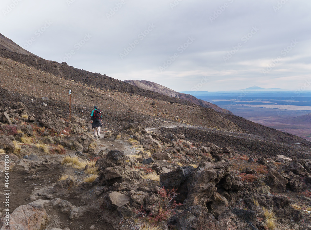 Hiking winding volcanic scree at Tongariro Alpine crossing. Mt Taranaki in the far distance. Tongariro National Park. New Zealand.