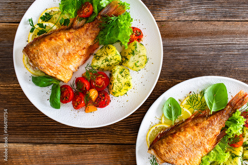 Fried atlantic redfish with boiled potatoes and tomato salad on wooden table