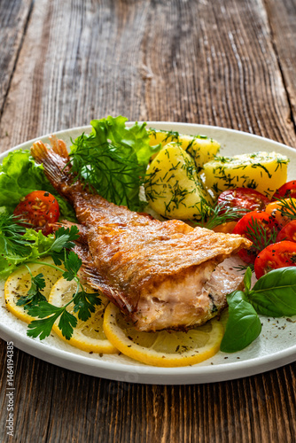Fried atlantic redfish with boiled potatoes and tomato salad on wooden table
