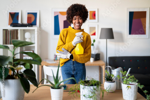 A smiling woman tends to her indoor garden. She is holding a spray bottle, ready to water her plants in her bright, modern home.