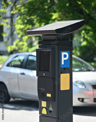 Solar-powered parking meter stands next to a parked car, showcasing modern urban infrastructure in daylight