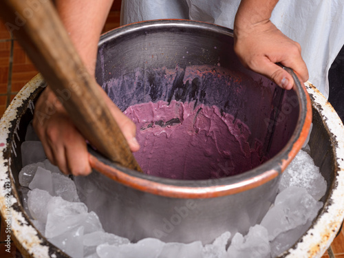 Foto Hands churn purple ice cream in a metal bowl surrounded by ice.