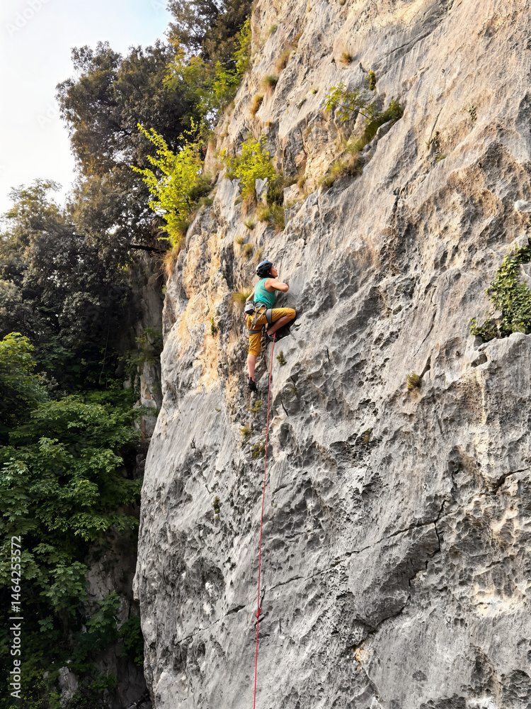 Obraz premium Female Climber Leading A Route In Yellow Pants At Nago Rock Climbing Area Near Arco, Lake Garda, Italy