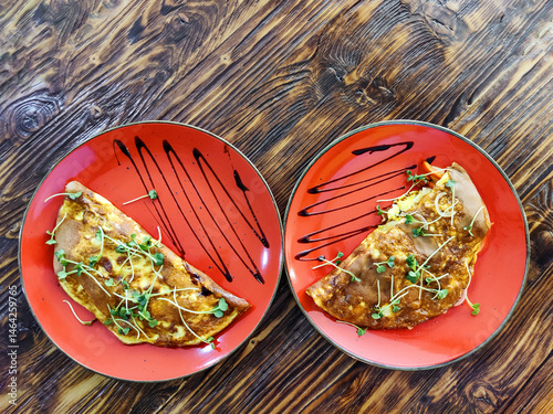 Omelette decorated with greens on red ceramic plates placed on dark surface of wooden vintage table. Simple, tasty and healthy food. Great breakfast. Top view. Close-up. Selective focus. Copy space.