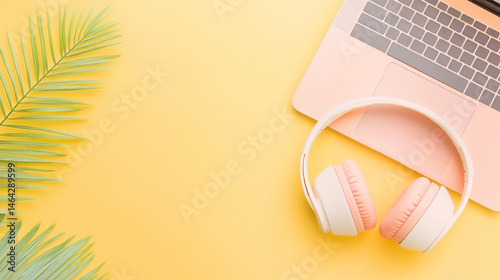 Top view of rose gold laptop, pastel headset and palm branch, soft pink, on bright yellow, for teenage girl, fun, summer remote work, background with copy space