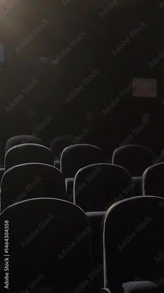 Survol de sièges de cinéma dans une salle obscure, la lumière vient dessiner les bords. Au format vertical 9:16. peut symboliser une sortie de film, ou ciné