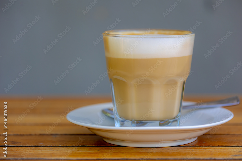 Coffee and barista concept, Selective focus of a milk coffee or cappuccino on wooden table, Hot cafe latte in glass mug and white saucer, Beverage background.
