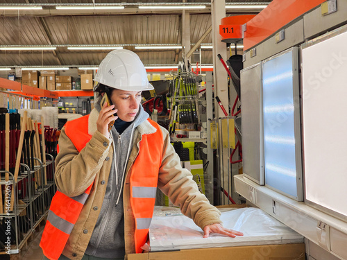  female builder, cranes unloading cargo, engineer designer, woman in orange construction helmet and orange vest, woman working in warehouse, building materials store, girl talking on phone