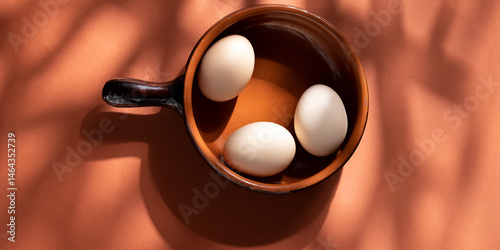 Handmade ceramic plates with home eggs on brown background. Terracotta objects, space for text. Genuine food concept.
