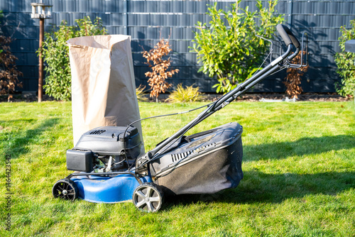 A lawn mower is sitting on the grass next to a bag of grass clippings