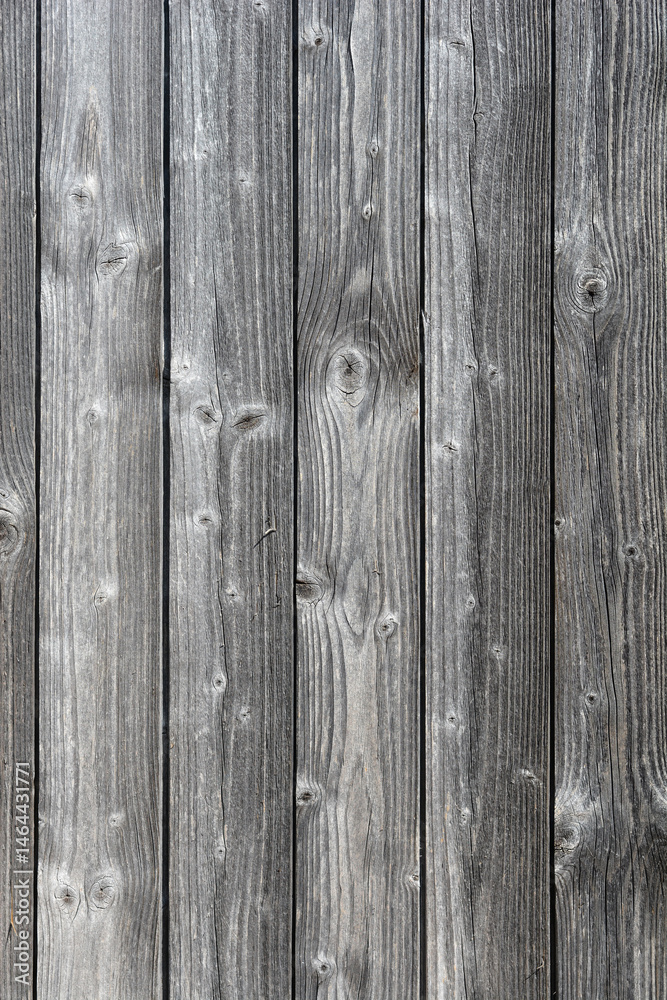 A close-up shows a textured surface of weathered, gray wooden planks arranged vertically with visible grain and knots