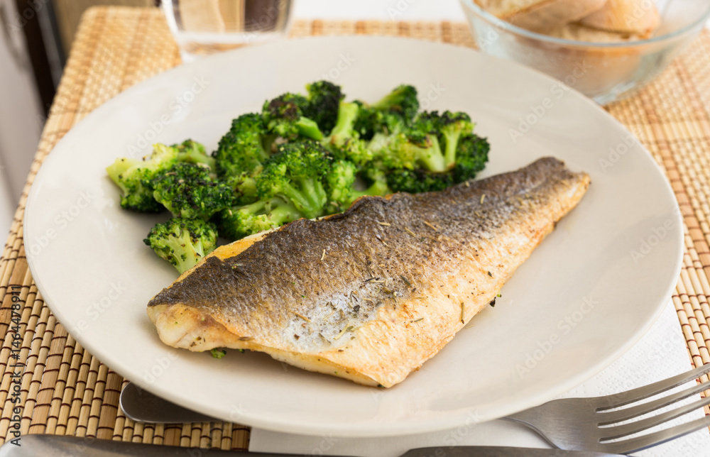 Fried fillet of sea bass with garnish of broccoli on black warm stone plate