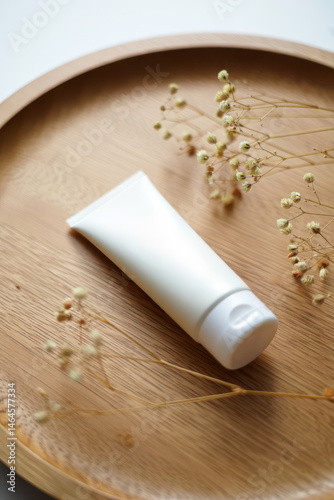 Obraz na płótnie A white cosmetic tube rests on a round wooden tray surrounded by delicate dried flowers. The arrangement creates a calming and minimalist atmosphere, emphasizing natural beauty w salonie