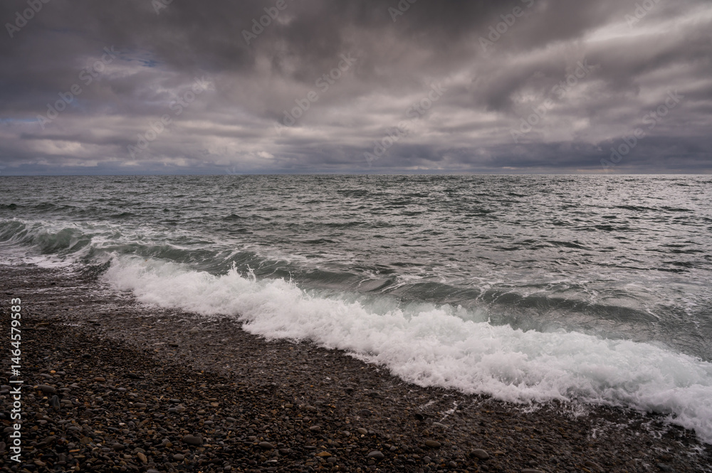 Sun between dark storm clouds over ocean. Dramatic seascape. Clouds and rain flurry over sea.