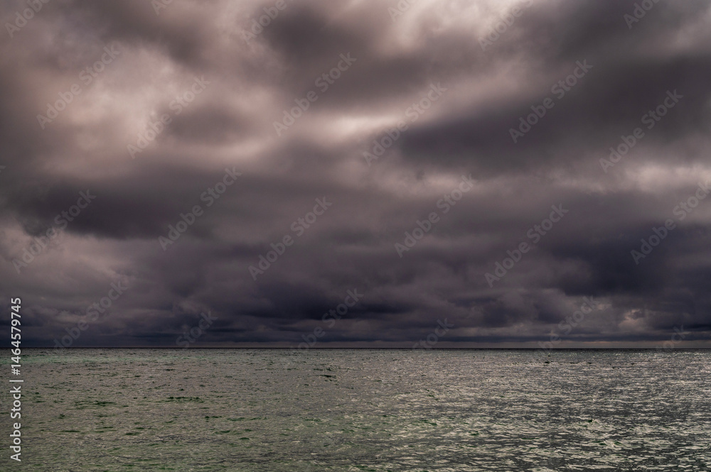 Sun between dark storm clouds over ocean. Dramatic seascape. Clouds and rain flurry over sea.