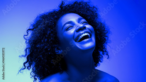 Lit in blue, an African American woman throws her head back in unrestrained laughter