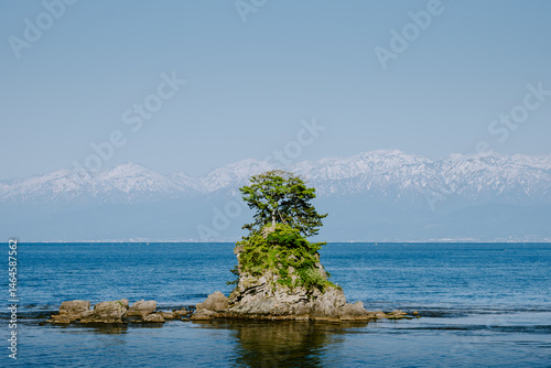 Amaharashi Rock Island and Snowy Tateyama Mountains under Clear Sky in Toyama, Japan