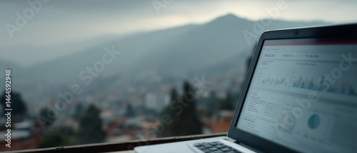 A laptop displaying data charts against a misty mountain backdrop, blending technology and nature.