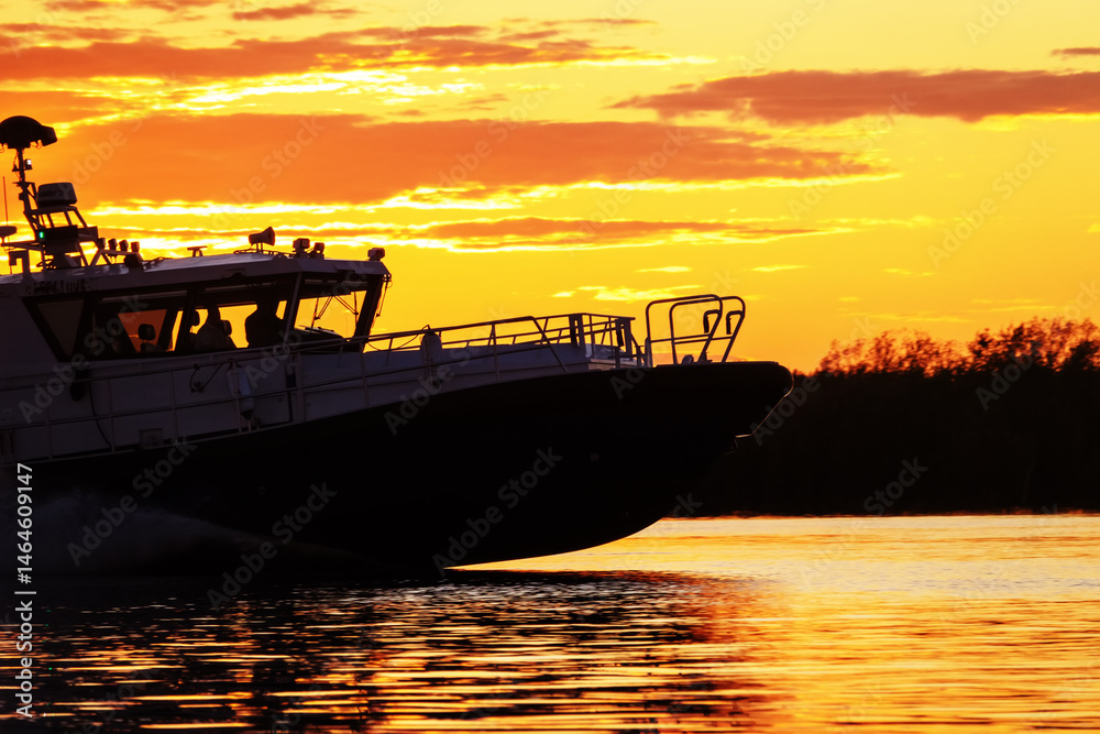 Naklejka premium A river yacht, a speedboat, is sailing fast along the river at sunset. Evening rest on the water, water-based recreation