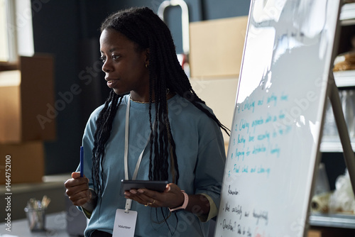 Teaching professional delivering engaging presentation in classroom, holding pen and tablet while explaining content on whiteboard. Attentive and focused on delivering message