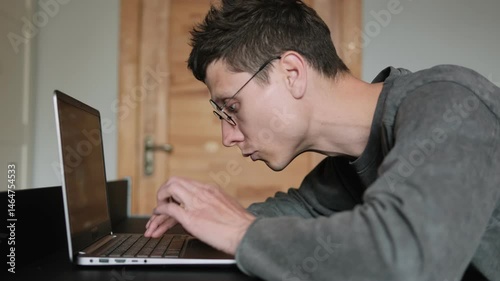 Neck discomfort from bad desk posture. Hunched back. Freelancer in glasses working with curved spine. Man slouching over laptop at home.