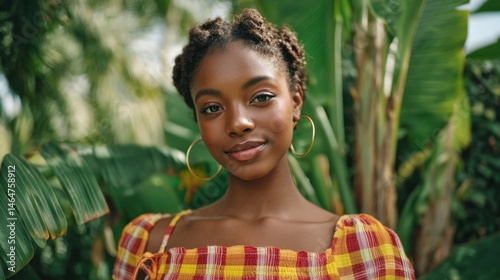 Obraz na płótnie Caribbean-American Heritage Month Smiling young african female in yellow and red top among lush green leaves w salonie