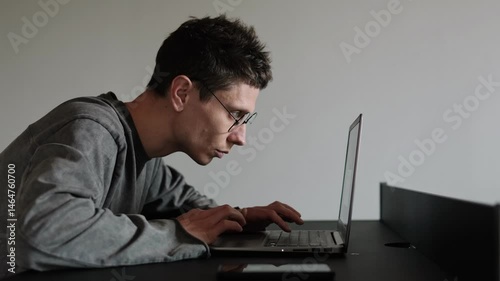 Hunched back from long hours at computer. Man in glasses sitting with bad posture at desk. Improper ergonomics during remote work. Office worker slouched at desk with laptop