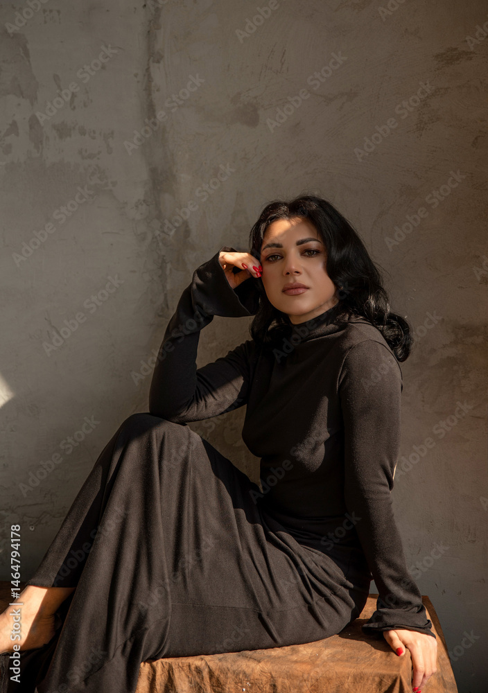 Naklejka premium Brunette in a black dress barefoot near a textured wall