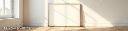 Sunlight streams onto empty horizontal frame against bright wall, resting on parquet floor , display, wood floor