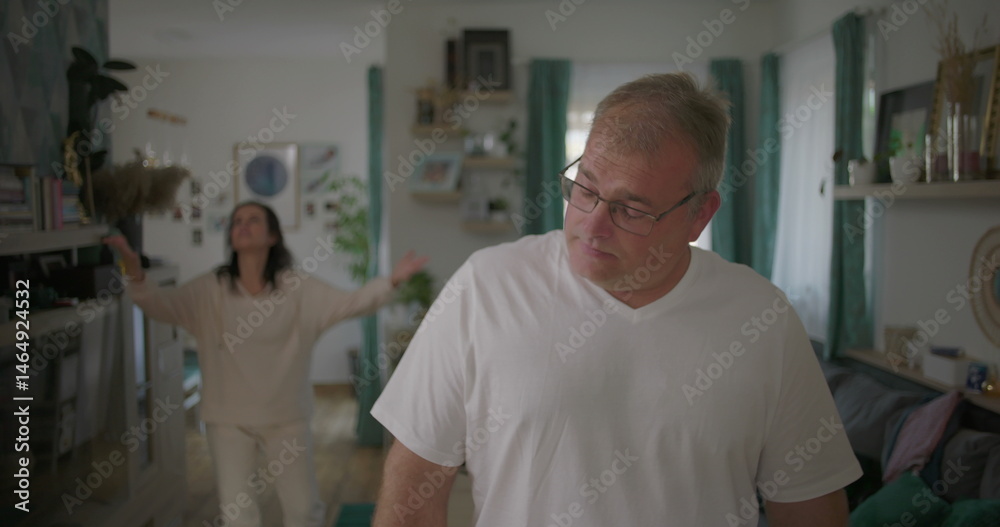 Obraz premium Man standing visibly upset during argument with woman in background, relationship tension in living room, emotional and dramatic moment of disagreement