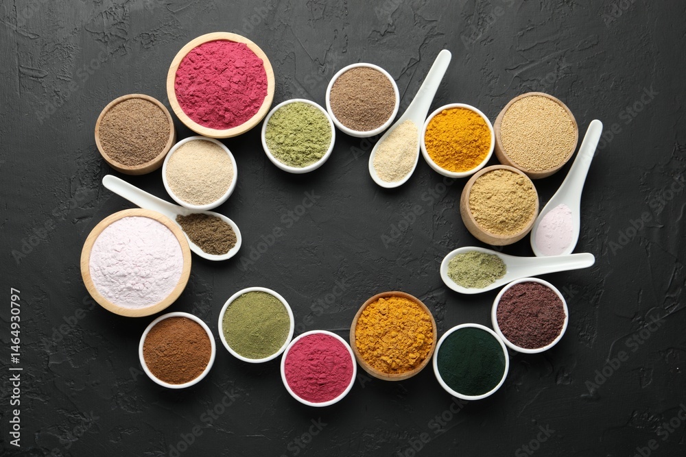 Fototapeta premium Frame of different superfood powders in bowls and spoons on dark textured table, flat lay. Space for text
