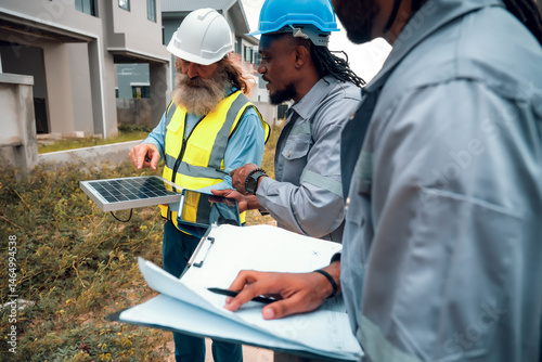 Construction engineers and their team are discussing the site preparation plan for installing solar panels, setting up the working system for an energy-saving housing project and exterior overview.