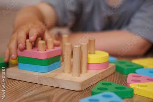 Close-up of child's hands playing with wooden educational toy-sorter. Horizontal photo. Concept of learning through play, fine motor skills and early childhood development