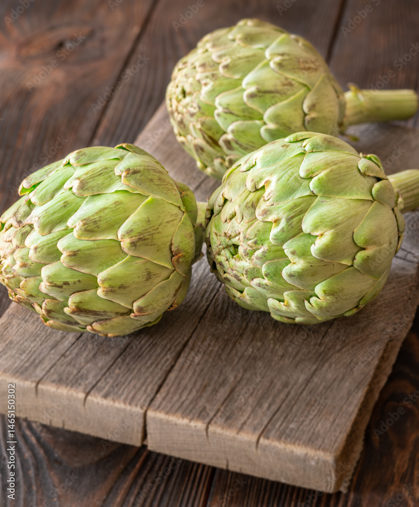 Fototapeta premium Fresh raw artichokes on vintage cutting board with rustic wooden background texture