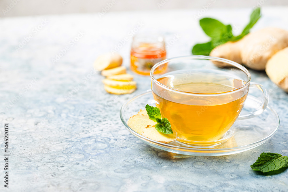 Ginger tea in a glass cup with lemon and mint on light background