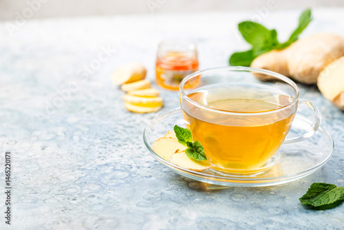 Ginger tea in a glass cup with lemon and mint on light background