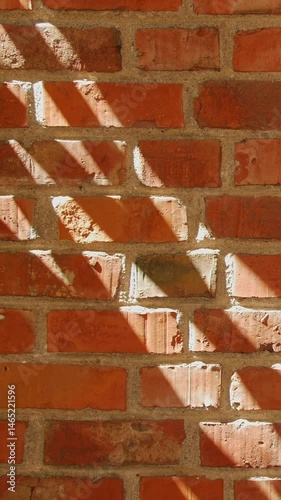 Diagonal shadows from sunlight highlight the texture and color of a red brick