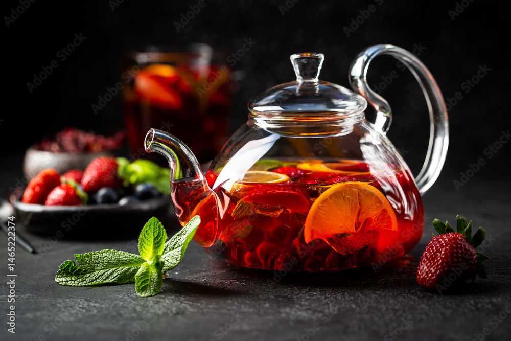 Fruit red tea with berries in glass teapot on black background