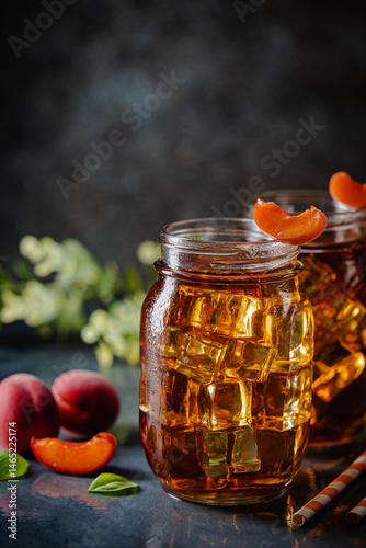 Obraz na płótnie Glass of peach or apricot iced tea with fruit slices against dark blue background w salonie