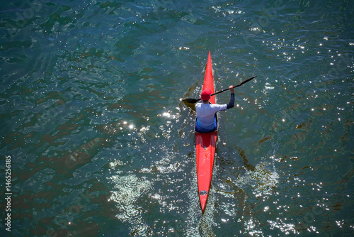 A boy kayaking on the water in a red kayak, viewed from above.
