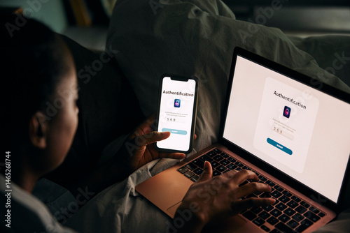 High angle view of woman accessing laptop through smart phone with authentication password while sitting in bedroom at h